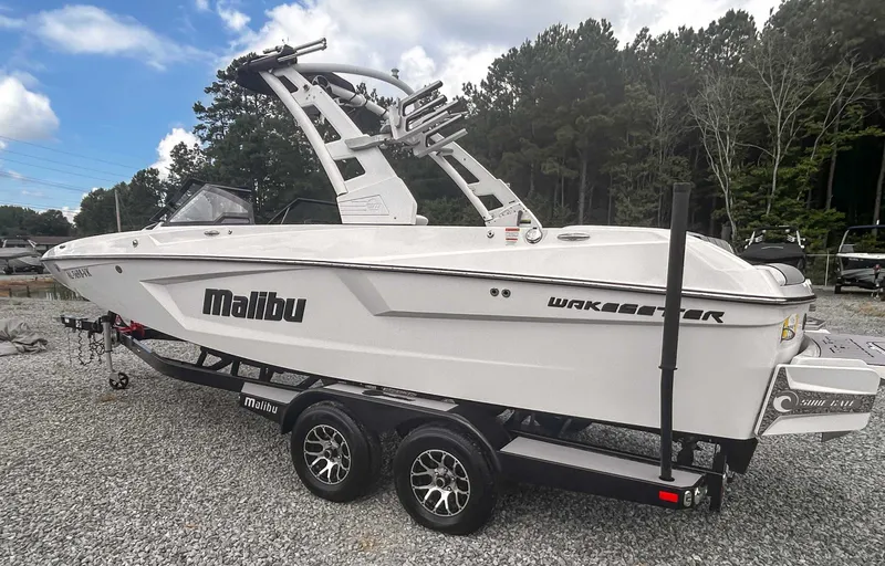 Slide: The Image of 2020 Malibu 23 MXZ boat on trailer, parked on gravel, surrounded by trees. - 6