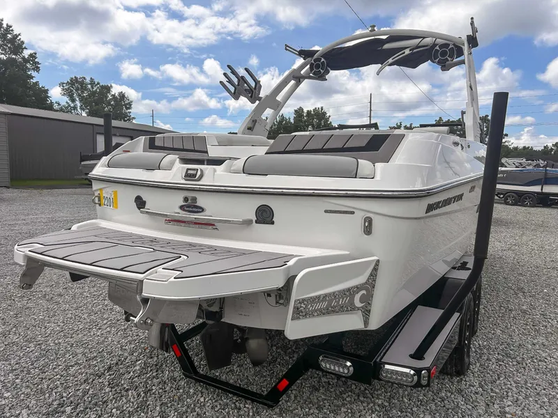 Slide: The Image of 2020 Malibu 23 MXZ boat on trailer, rear view, parked on gravel lot. - 8