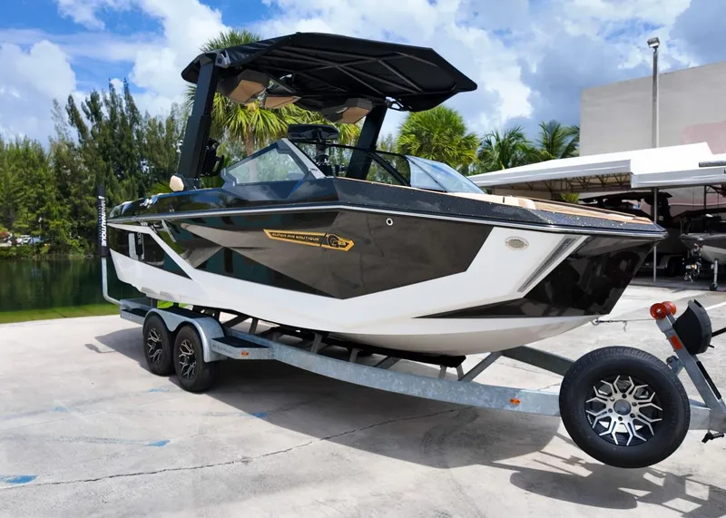 Slide: The Image of 2025 Nautique G23 boat on trailer, sleek black and white design, parked outdoors. - 1