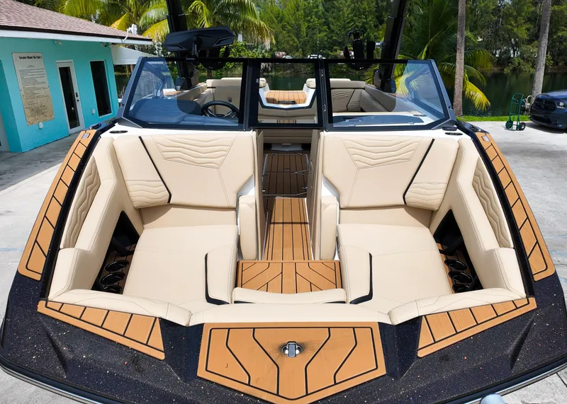 Slide: The Image of 2025 Nautique G23 boat interior with beige seating and wood accents, docked near a turquoise building. - 16