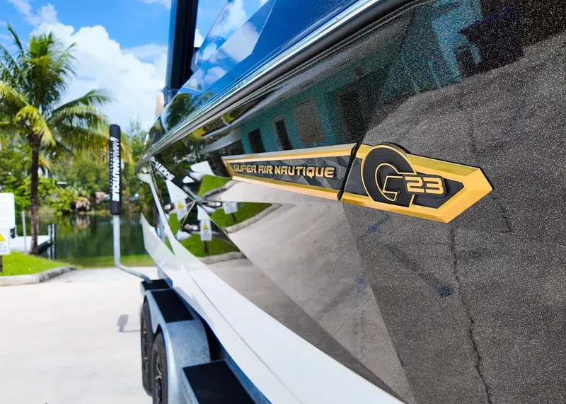 Slide: The Image of 2025 Nautique G23 boat with sleek design and gold emblem, parked near tropical scenery. - 9
