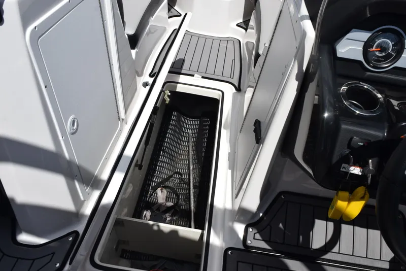 Slide: The Image of 2018 Yamaha Boats 212X interior storage compartment with open hatch and dashboard view. - 17