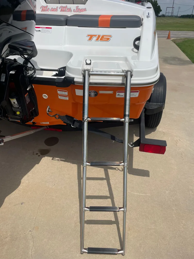 Slide: The Image of 2020 Tahoe T16 boat with ladder, orange and white design, parked on concrete. - 4