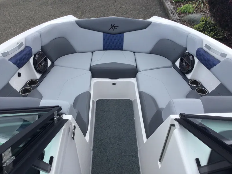 Slide: The Image of 2022 MasterCraft XT24 boat interior with gray and blue seating, cup holders, and speakers. - 21