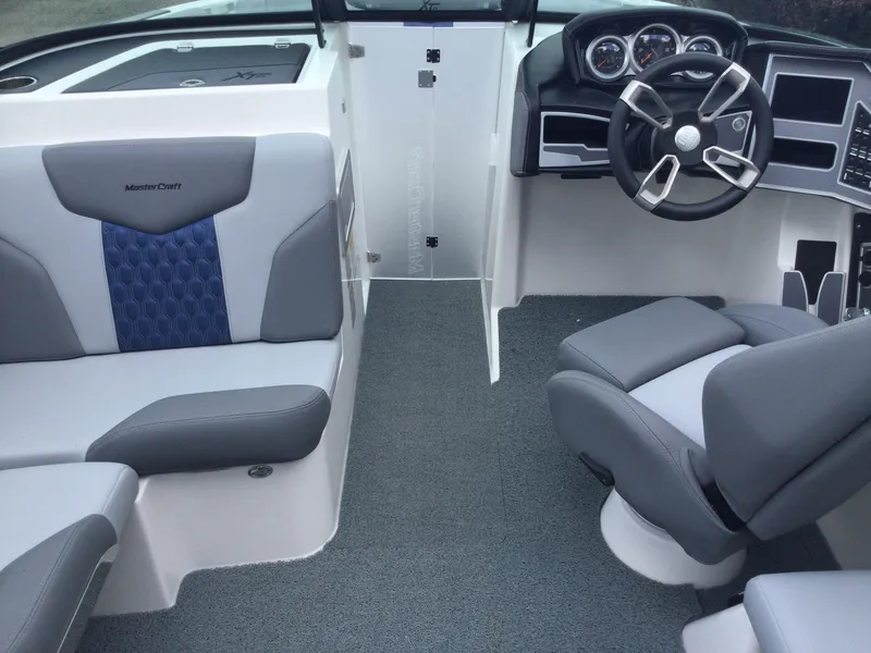 Slide: The Image of 2022 MasterCraft XT24 boat interior with gray and blue seating, modern dashboard, and steering wheel. - 30