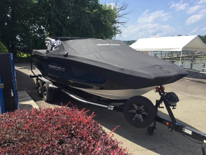Slide: The Image of 2022 MasterCraft XT24 boat covered on trailer near waterfront. - 4
