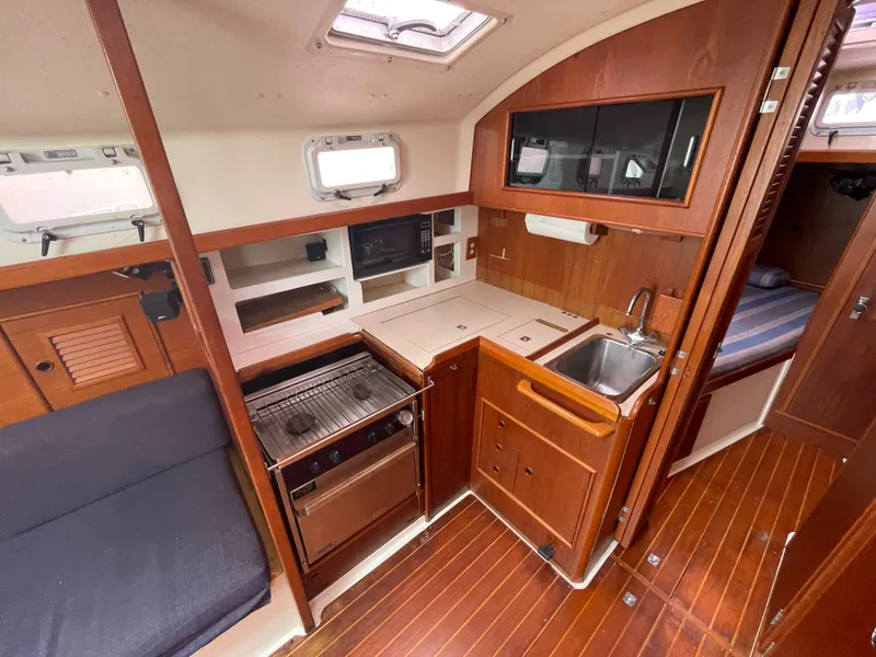 Slide: The Image of 1987 Nonsuch 30 Ultra yacht interior with wood finish, compact kitchen, and cozy seating area. - 14