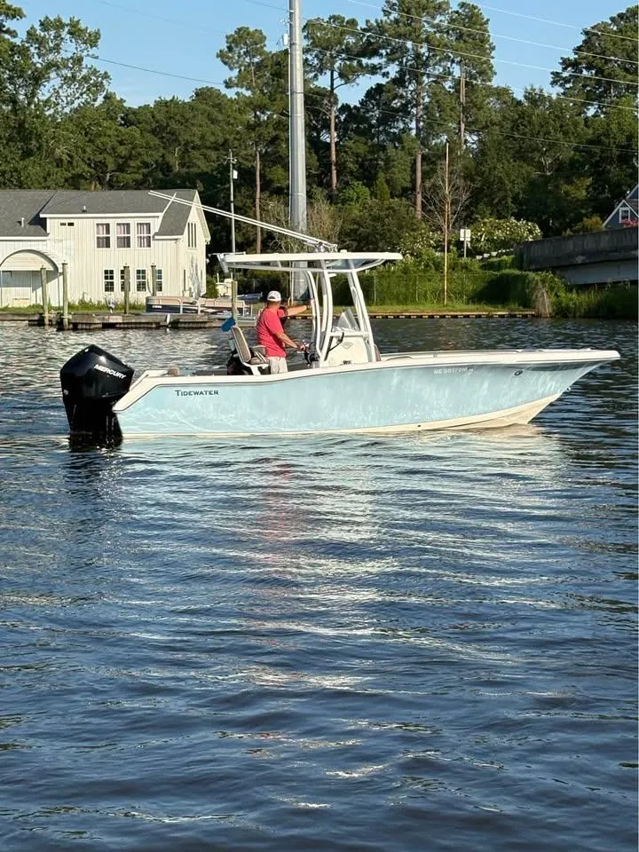 Slide: The Image of 2019 Tidewater 220 LXF boat on calm water near a house and trees. - 2