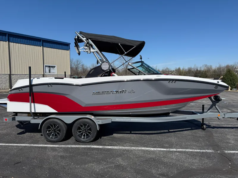 Slide: The Image of 2025 MasterCraft NXT22 boat on trailer, gray and red design, parked outdoors. - 3