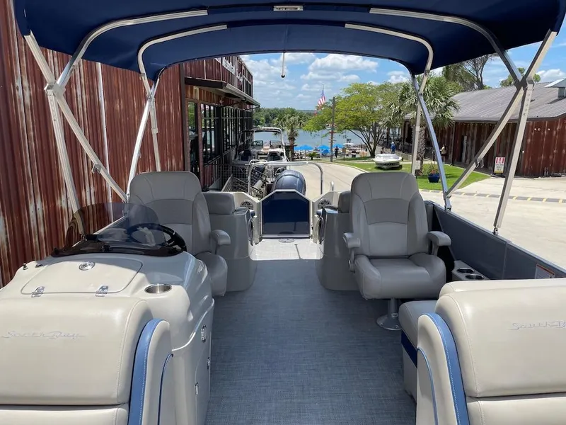 Slide: The Image of 2017 South Bay 500 pontoon boat interior with seating and canopy, docked near a lakeside view. - 13