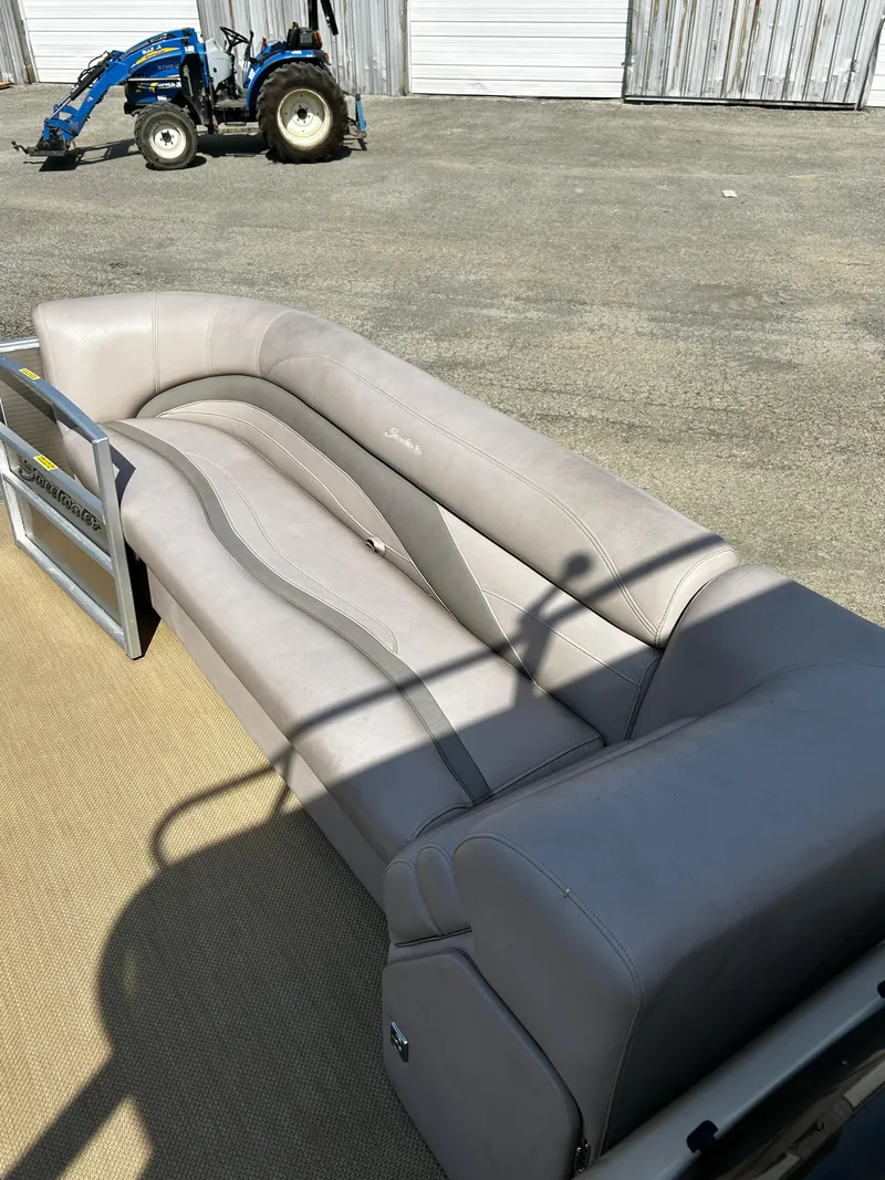 Slide: The Image of Sweetwater Premium Edition 240 boat interior with beige seating, 2015 model, parked near a blue tractor. - 6