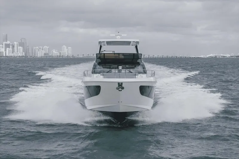 Slide: The Image of 2025 Cruisers Yachts 57 Fly cruising on open water with city skyline in background. - 3