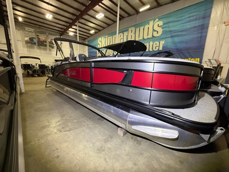 Slide: The Image of A sleek Barletta Lusso 23 QCSS pontoon boat with red and black design in a warehouse. - 0