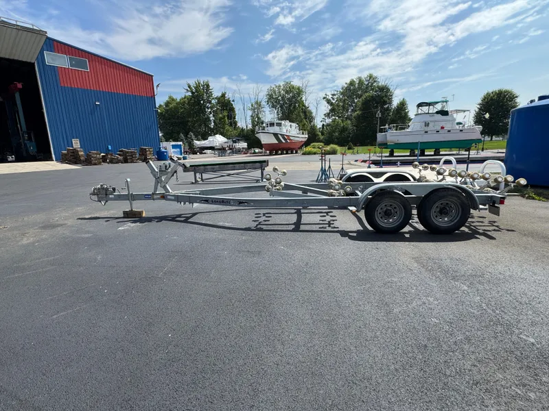 Slide: The Image of Boat trailer parked outside, near a blue building, with boats in the background. - 32