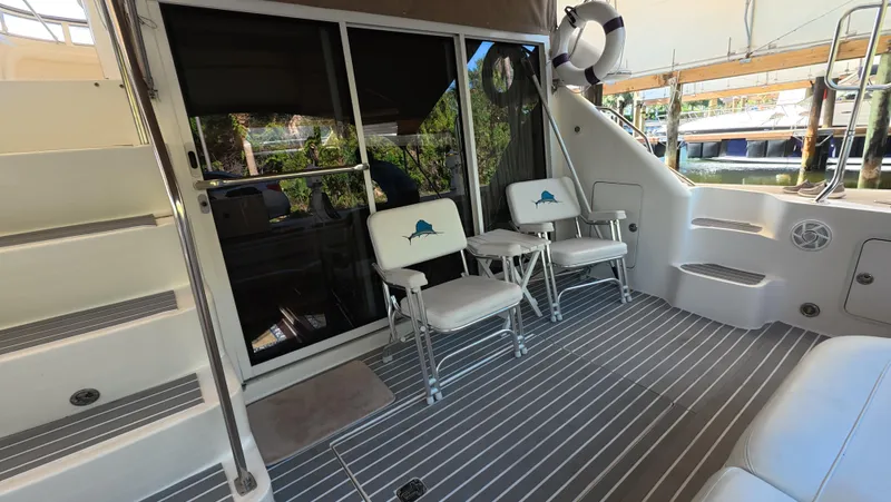 Slide: The Image of 2001 Sea Ray 450 Express Bridge yacht deck with chairs and stairs, docked by water. - 22