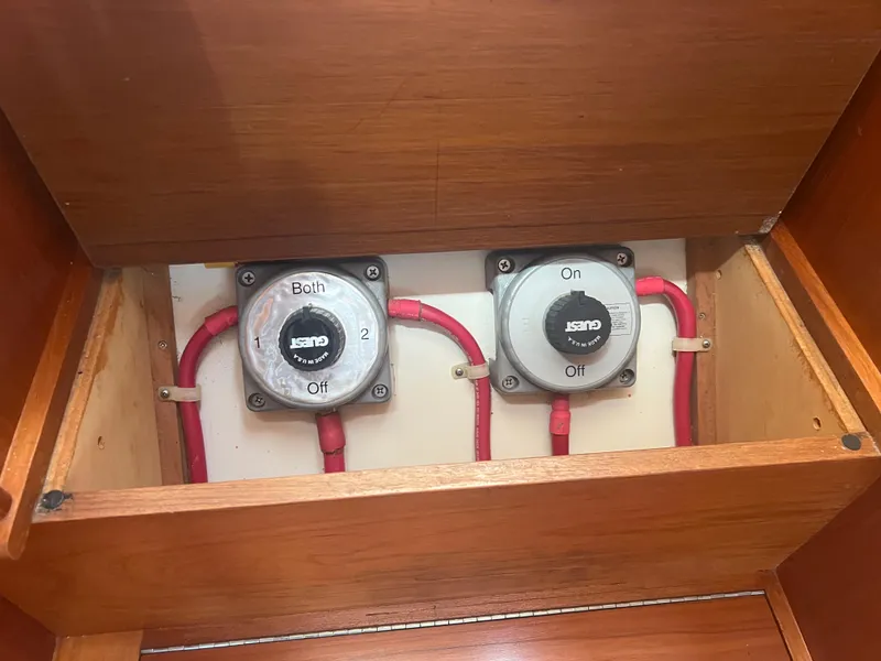 Slide: The Image of Battery switches in a 1998 Cherubini Independence boat, featuring red cables and wooden paneling. - 47