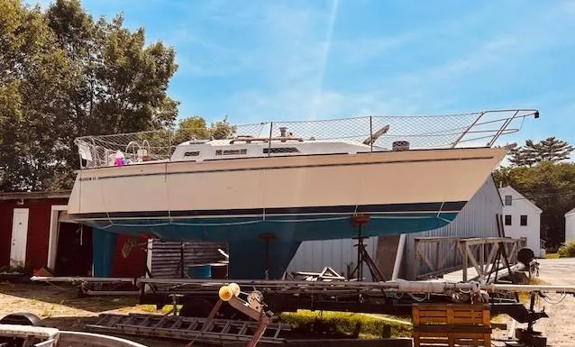The Image of 1986 Pearson 28 sailboat on a trailer, surrounded by trees and buildings. - 0
