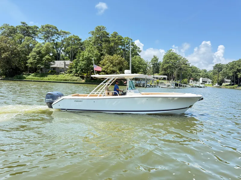 Slide: The Image of 2014 Pursuit ST 310 Sport boat cruising on a scenic lake with lush greenery. - 2