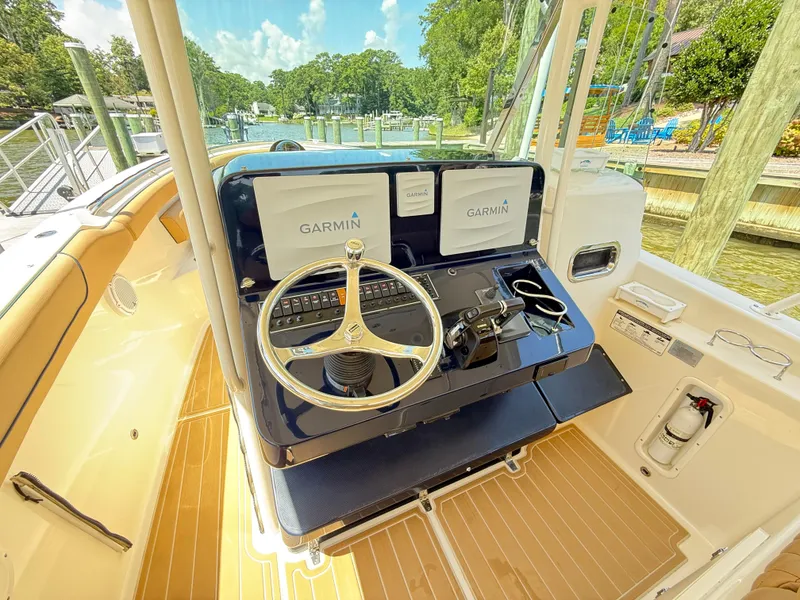 Slide: The Image of 2014 Pursuit ST 310 Sport boat helm with Garmin navigation, docked by a scenic waterfront. - 29