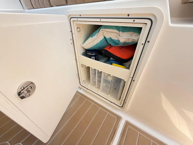 Slide: The Image of Open storage compartment on 2014 Pursuit ST 310 Sport boat, containing safety and utility items. - 45