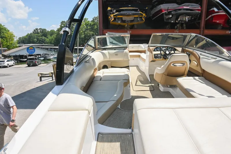 Slide: The Image of 2015 Cobalt 220 boat interior with beige seating and dashboard, parked at a marina. - 13