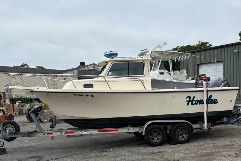 Slide: The Image of 2012 Parker 2120 Sport Cabin boat on trailer, parked outdoors near industrial buildings. - 2