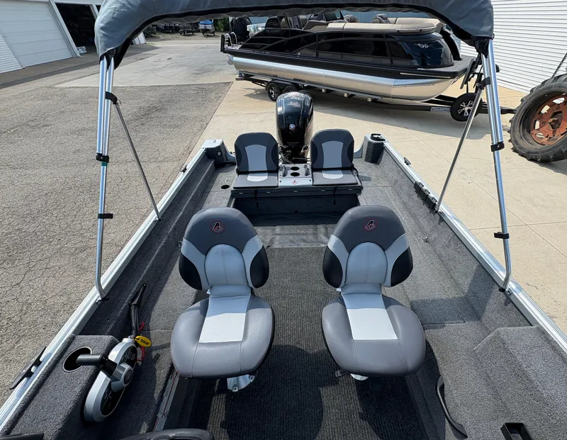 Slide: The Image of 2018 Alumacraft Voyageur 175 Sport interior with seating and steering wheel, parked near a pontoon boat. - 23