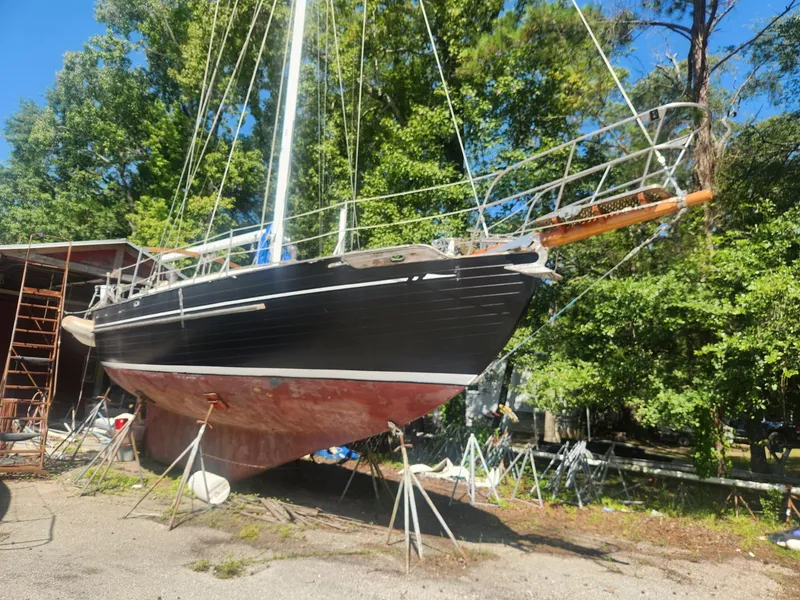 The Image of 1976 Tayana 37 sailboat on stands, surrounded by trees and a clear blue sky. - 0