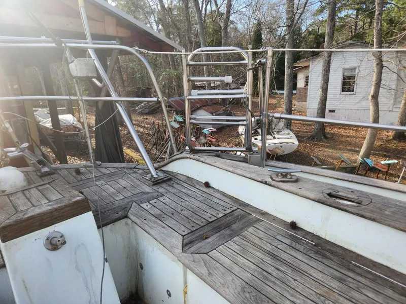 Slide: The Image of 1976 Tayana 37 sailboat deck with wooden flooring, surrounded by trees and outdoor equipment. - 17