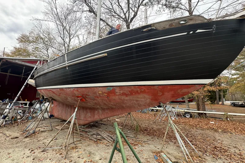 Slide: The Image of 1976 Tayana 37 sailboat on stands, undergoing maintenance in a wooded area. - 39