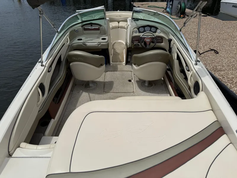 Slide: The Image of 2004 Sea Ray 220 Select boat interior with beige seating and dashboard, docked by the water. - 15