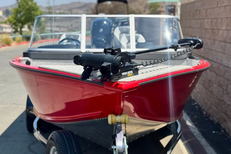 Slide: The Image of Red Apex Outlander V2010 boat, 2024 model, with Minn Kota trolling motor, parked outdoors. - 2