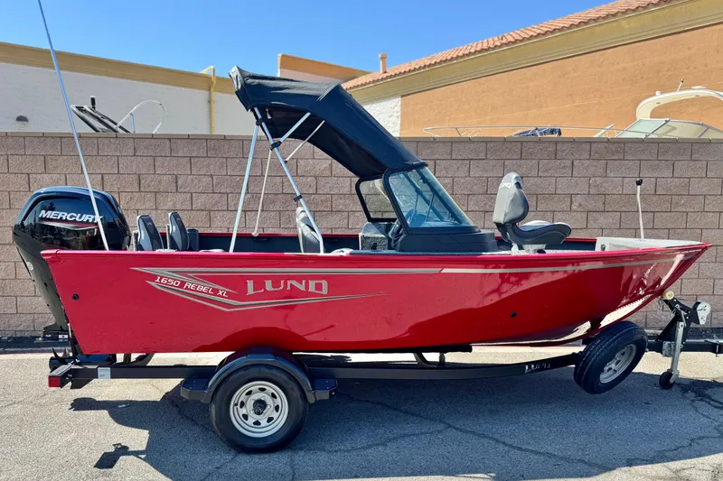 The Image of 2024 Lund 1650 Rebel XL Sport boat, red exterior, on trailer, with Mercury outboard motor. - 0