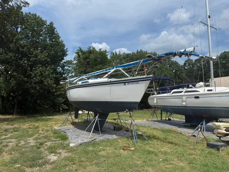 The Image of 1986 Hunter 28.5 sailboat on stands, surrounded by trees and grass. - 1