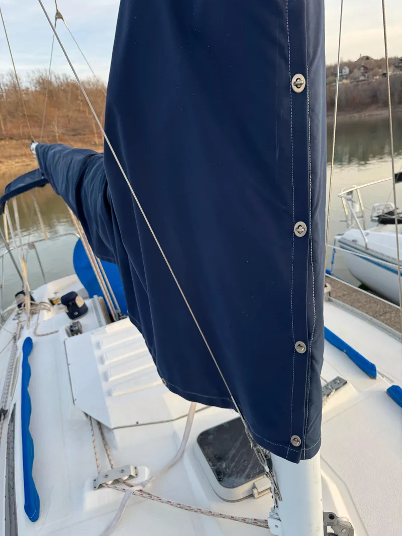 Slide: The Image of 1986 Hunter 28.5 sailboat with blue sail cover, docked by a calm river. - 16