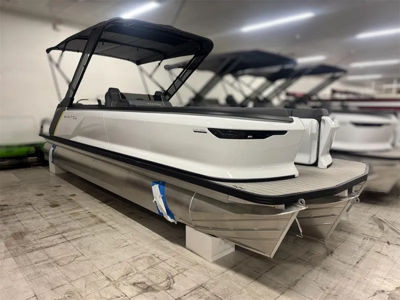 Slide: The Image of 2025 Manitou Explore 24 Navigator pontoon boat in showroom, featuring sleek design and modern amenities. - 2
