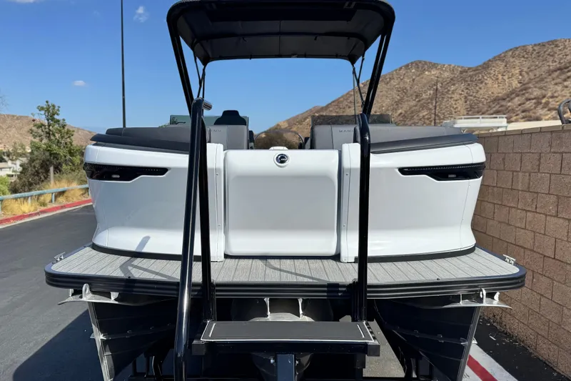 Slide: The Image of 2025 Manitou Explore 24 Navigator boat, rear view, parked outdoors with scenic background. - 2