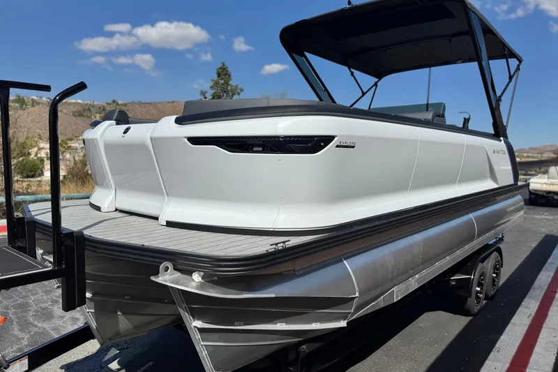 Slide: The Image of 2025 Manitou Explore 24 Navigator pontoon boat on trailer under clear sky. - 3