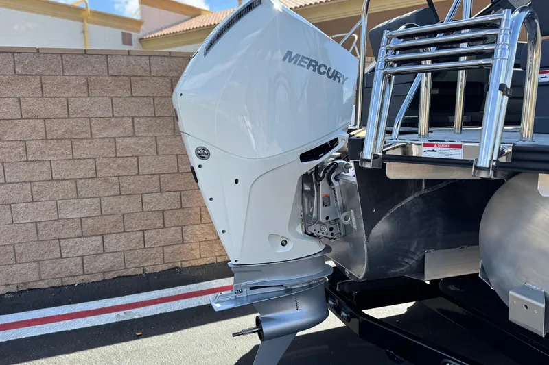 Slide: The Image of 2025 Manitou Explore 24 Navigator with Mercury outboard motor, parked near brick wall. - 7