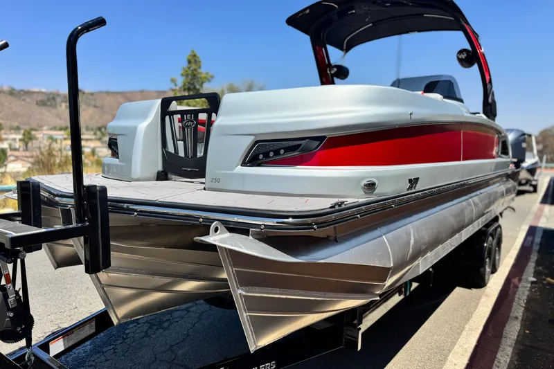 Slide: The Image of 2023 Manitou 25 XT RFXW pontoon boat on trailer, featuring sleek design and red accents. - 3