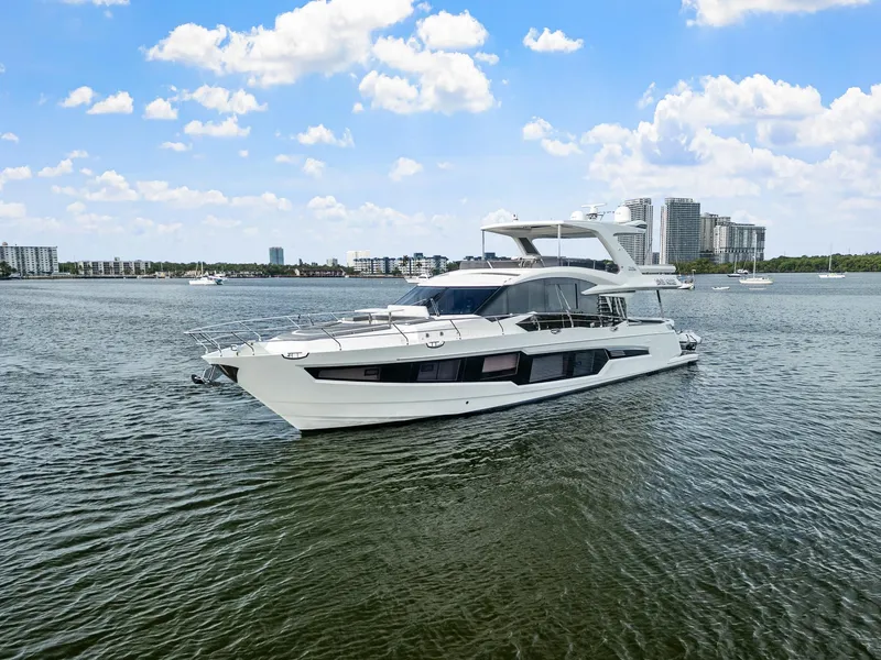 The Image of 2021 Galeon 680 Fly yacht cruising on a calm waterway with cityscape backdrop. - 25