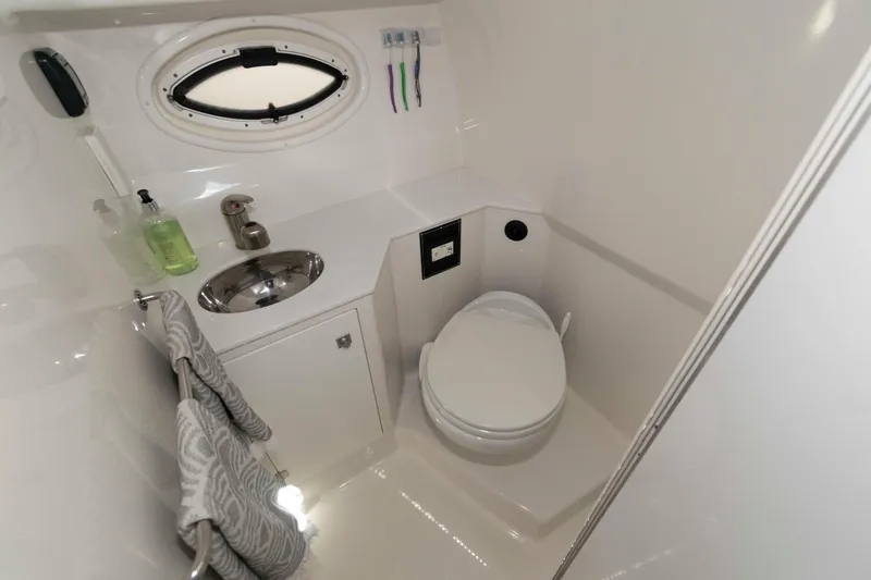Slide: The Image of 2018 Monterey 295 Sport Yacht bathroom with sink, toilet, and porthole window. - 17