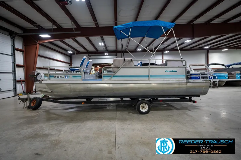 Slide: The Image of 1988 Landau 20 Adventurer pontoon boat with blue canopy in indoor showroom. - 2