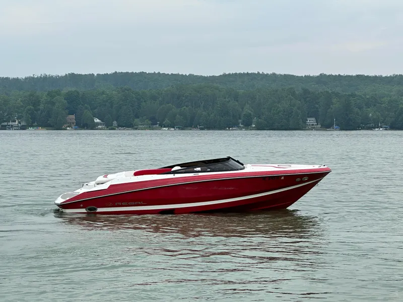 The Image of 2008 Regal 2200 RS boat on a calm lake with forested shoreline. - 2