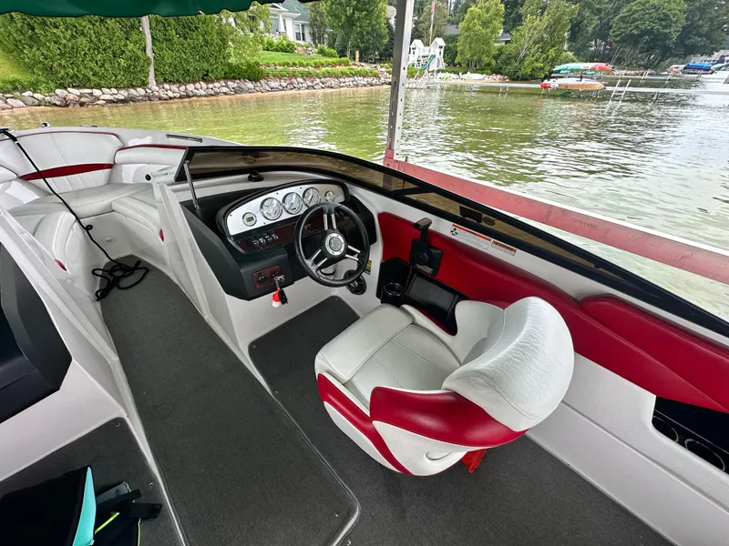 Slide: The Image of 2008 Regal 2200 RS boat interior with red and white seating, docked by a scenic lakeside. - 7