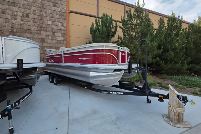The Image of 2025 Sun Tracker Party Barge 24 DLX pontoon boat on trailer, parked outdoors. - 0