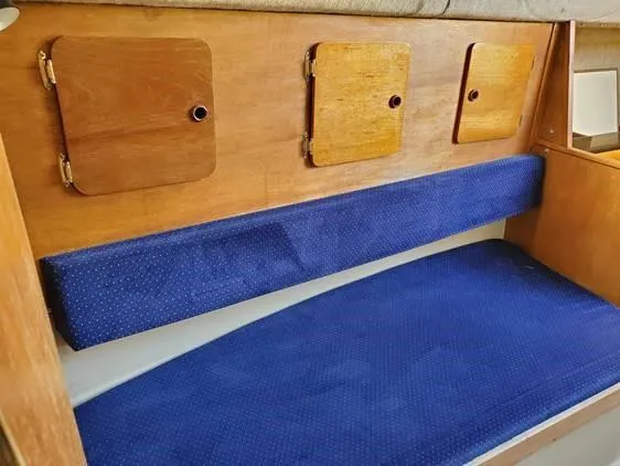Slide: The Image of Interior of 1987 O'Day 272 sailboat with blue cushioned seating and wooden storage panels. - 26