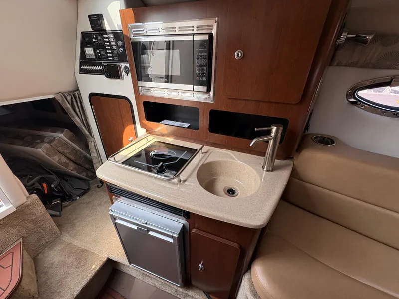 Slide: The Image of 2019 Crownline 264 CR boat interior with kitchenette, featuring sink, stove, and microwave. - 13