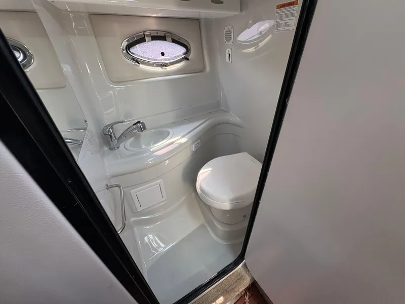 Slide: The Image of 2019 Crownline 264 CR boat bathroom with sink, toilet, and porthole window. - 15