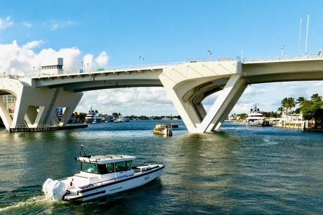 Slide: The Image of 2023 Axopar 28 CABIN boat cruising under a modern bridge on a sunny day. - 4